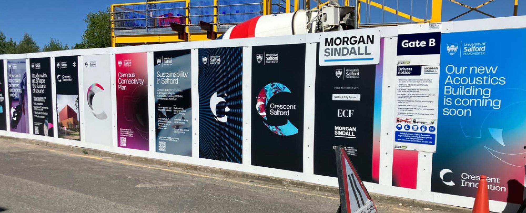Long construction hoarding at the University of Salford for the construction of its new Acoustics Building.