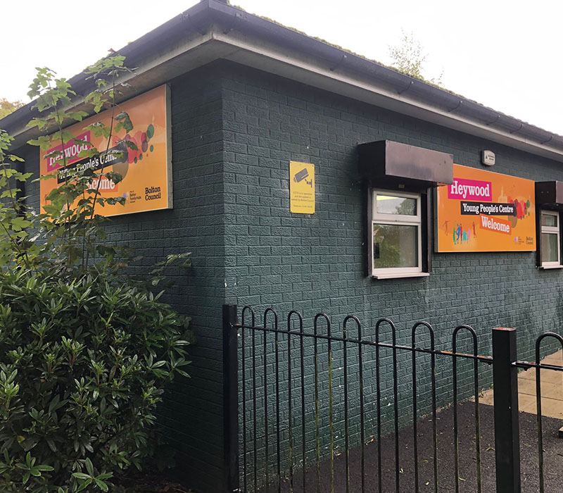 Outside the Heywood Young Peoples Centres green brick building with two welcome signs created by Impression