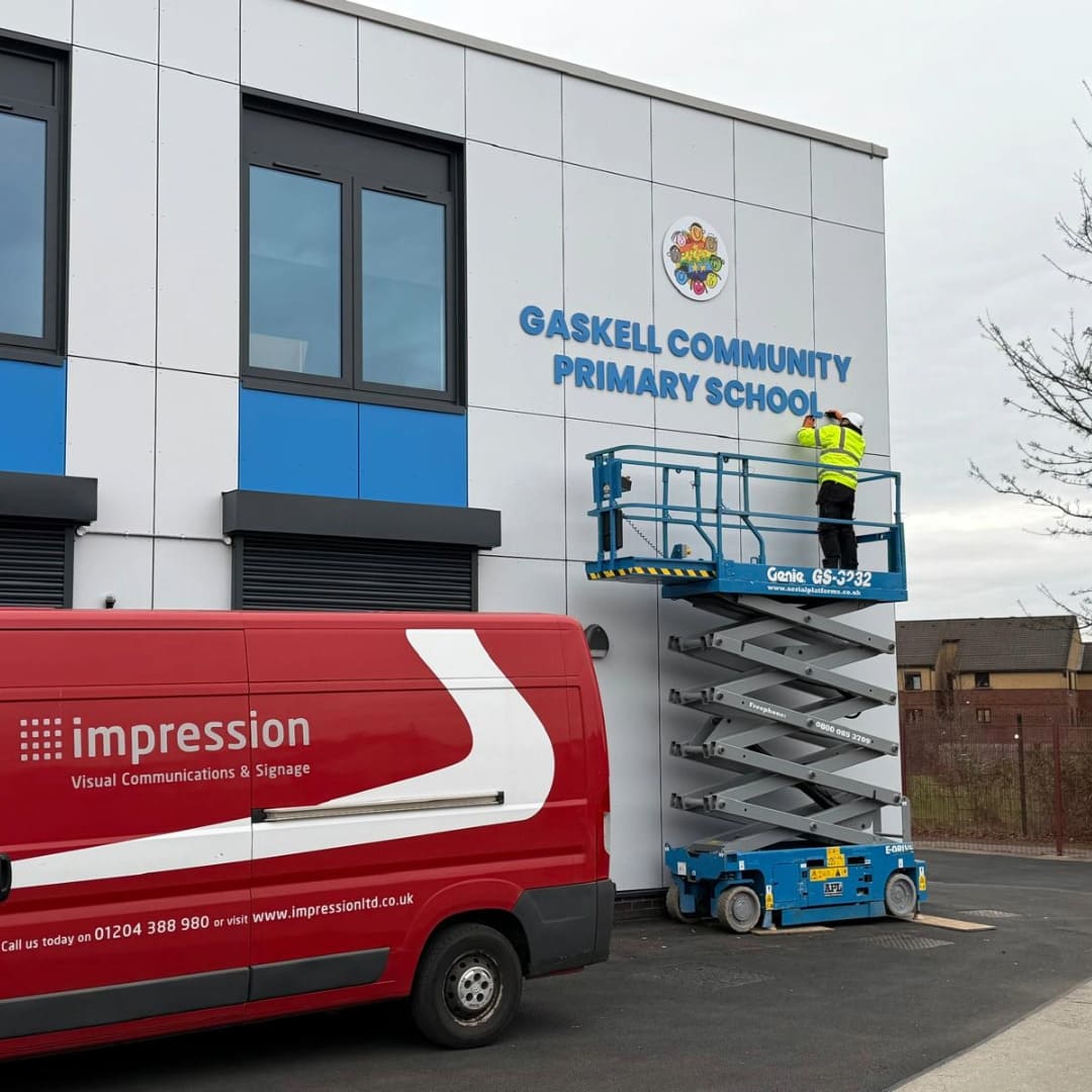 Impressions Deliver team installing letter signage using a scissor lift at Gaskell Community Primary School in Bolton