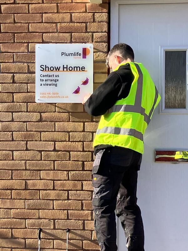 Hardwearing acrylic wall sign at the entrance of a show home being installed by Impressionâs âDeliverâ installation team, printed and manufactured in-house to make a smart and durable visual impact that attracts attention at this new Plumlife site